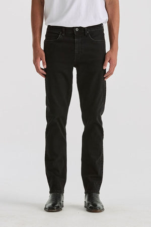 A person, visible from chest down, stands facing forward in a white T-shirt, black shoes, and the Lee Originals L100 Slim Jean against a plain white background, highlighting the timeless style of the jeans.