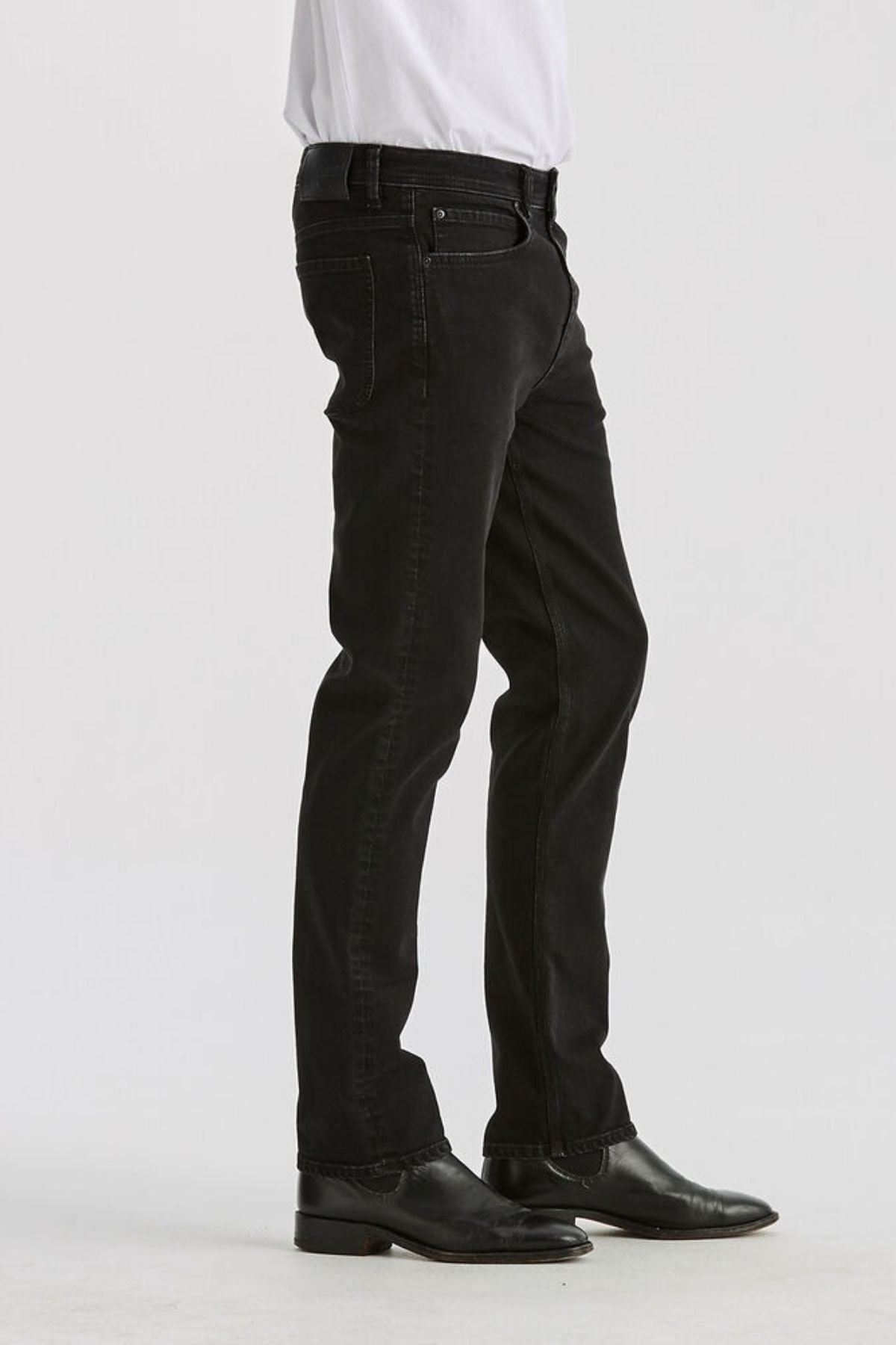 A person in a white shirt, Lee Originals L100 Slim Jean, and black dress shoes stands sideways against a plain white background—a look that embodies timeless style.