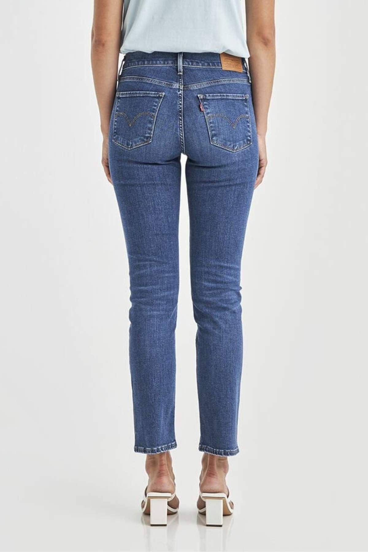A person is shown from the back against a plain white background wearing Levis 312 Shaping Slim Jeans, which feature stretch fabric, two back pockets, and a light brown waistband patch, paired with white heeled sandals.