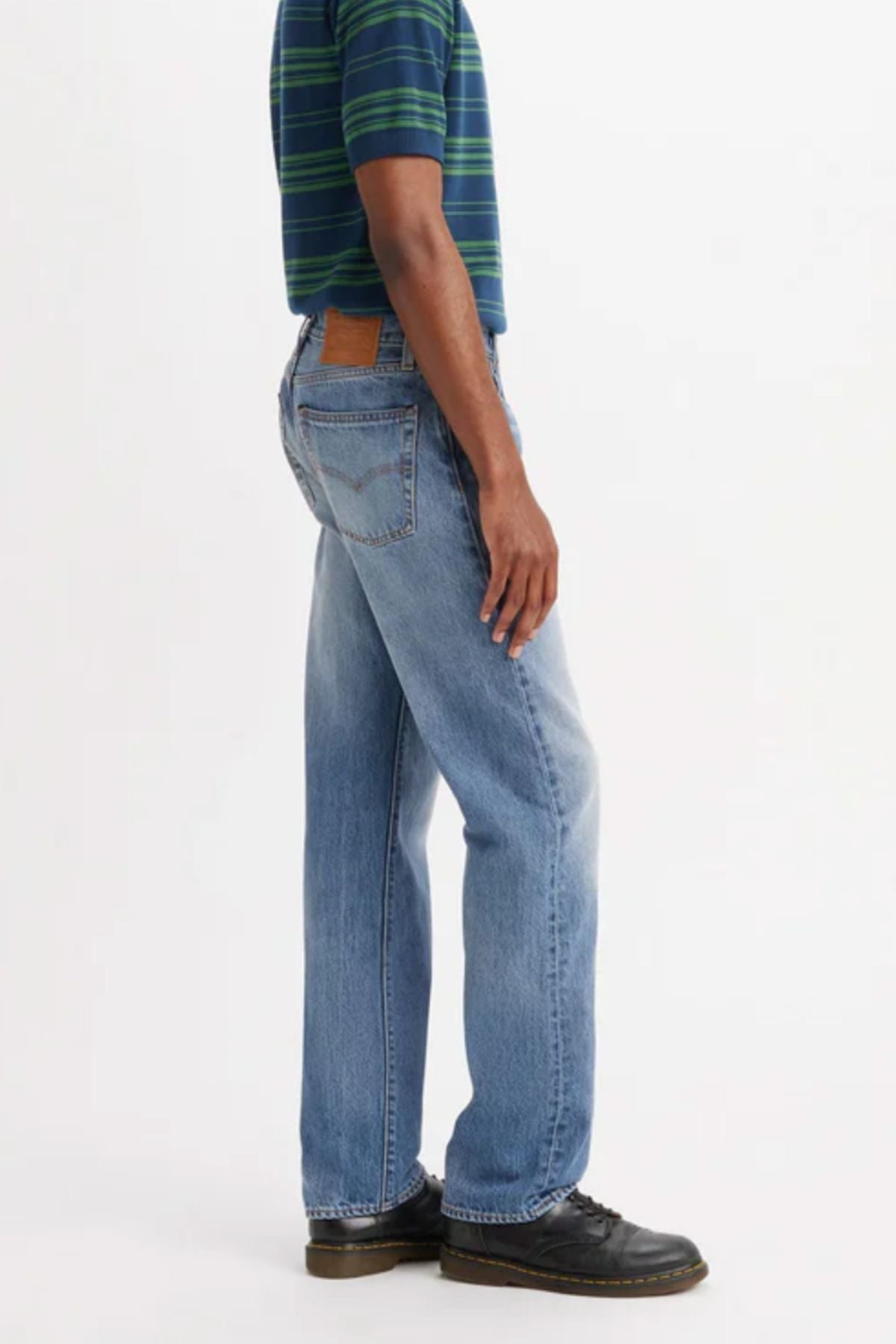 A person wearing a green and blue striped shirt, Levis 555 Relaxed Straight Jean, and black shoes stands sideways against a plain white background.