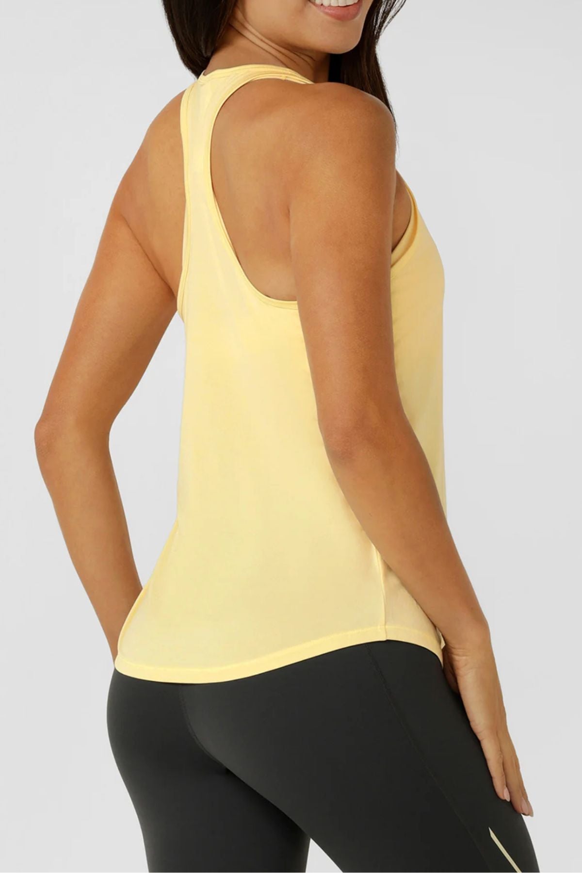 A woman stands sideways and smiles at the camera, wearing the Lorna Jane Amy Dynamic Active Tank and black leggings against a plain light background.