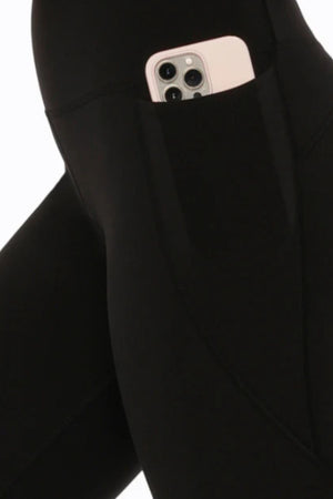 A close-up of Lorna Jane Amy Phone Pocket 3/4 Tech Leggings in black, featuring a side pocket holding a smartphone in a white or light-colored case.