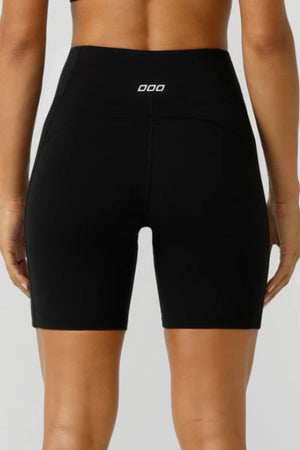 A person wearing high-waisted, black Lorna Jane Amy Phone Pocket Tech Bike Shorts with a small white logo on the waistband, shown from the back against a neutral background.