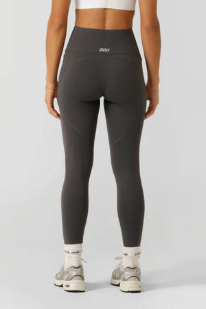 A person in a white sports bra, Lorna Jane Amy Thermal Phone Pocket Full Length Leggings in dark gray, white socks, and gray sneakers stands with their back to the camera—ideal for cold-weather workouts.