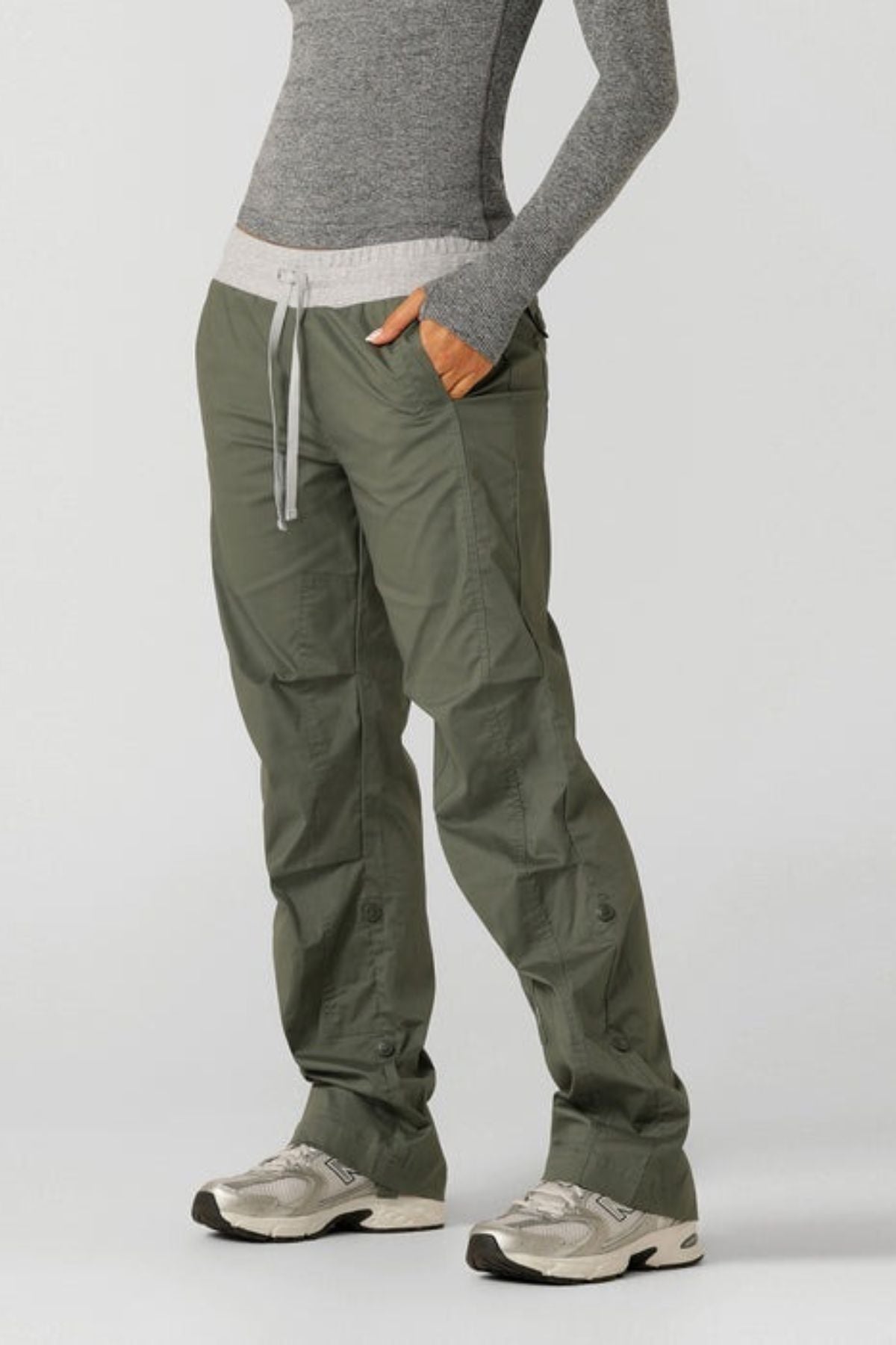 Someone stands with hands in pockets, wearing a fitted gray long-sleeve shirt and Lorna Jane Flashdance Pant with an adjustable waist, paired with white athletic shoes, against a plain light background.