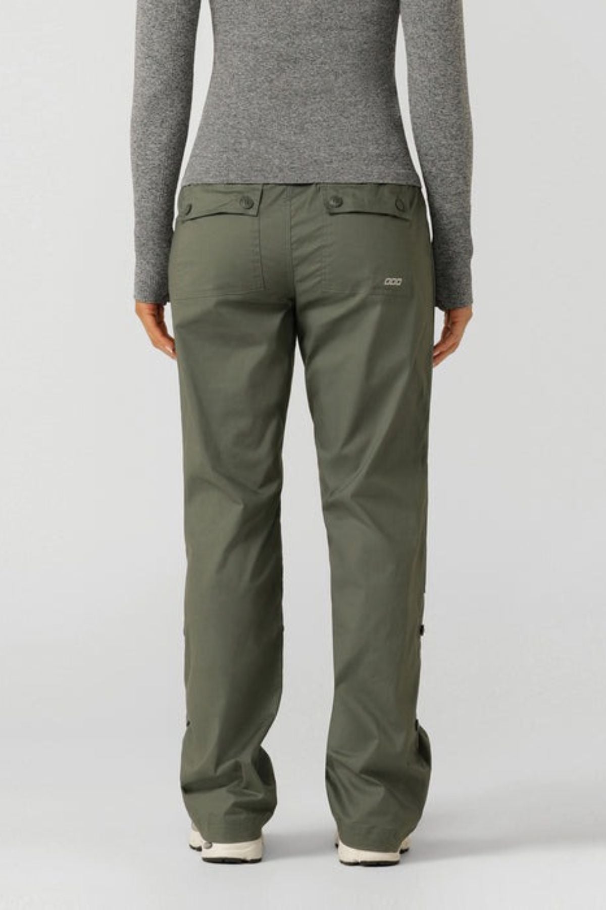 A person stands with their back to the camera, wearing olive green Lorna Jane Flashdance Pant with an adjustable waist and a fitted gray long-sleeve top, set against a plain light background.