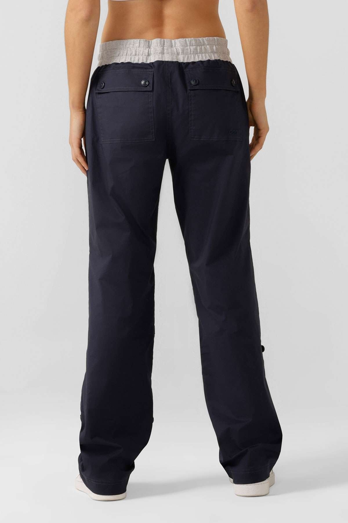 A person faces away from the camera, wearing Lorna Jane Flashdance Pant in navy blue with reinforced seams, buttoned back pockets, a light gray waistband, and winter fabrication visible on their lower back and legs.