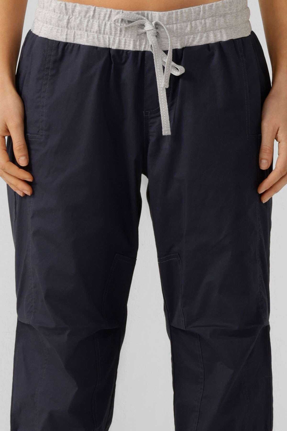 A person wears Lorna Jane Flashdance Pant in navy blue, with a light gray waistband and winter fabrication, shown from waist to mid-thigh, hands relaxed at their sides.
