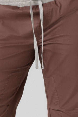 Close-up of a person wearing brown Lorna Jane Flashdance Pant with adjustable elastic waist, paired with a light gray shirt. The smooth fabric, visible stitching, and pockets make it perfect for winter. Waist and upper legs are shown.