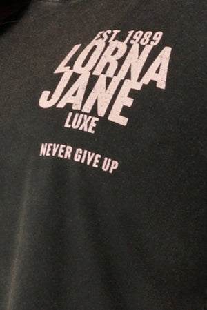 Close-up of a black Lorna Jane Heritage Inspiration Relaxed T-Shirt with vintage wash, featuring white text: "EST. 1989 LORNA JANE LUXE NEVER GIVE UP.