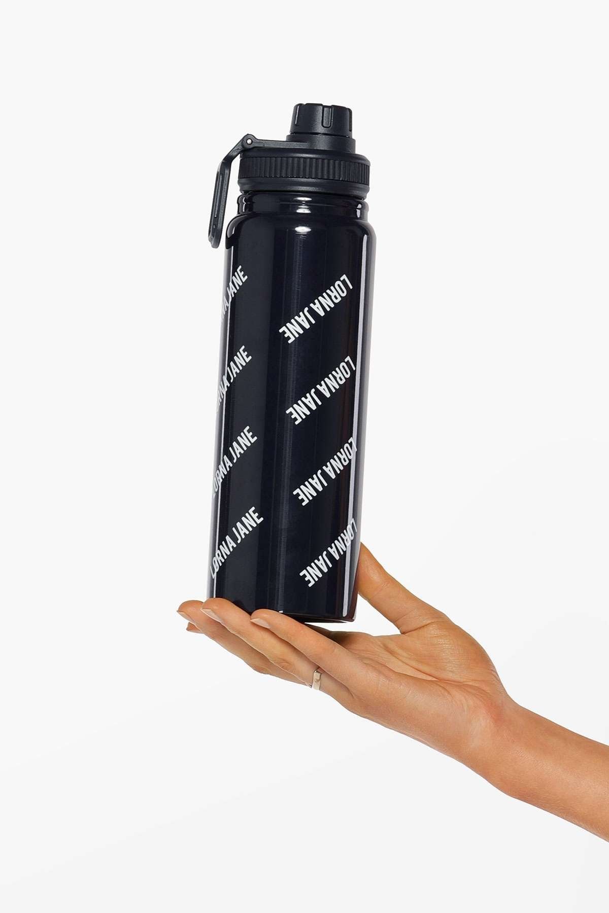A hand with a silver index finger ring holds the Lorna Jane Iconic Insulated Water Bottle, featuring a black design, flip-top lid, secure silicone seal, and "LORNA JANE" printed in white diagonal text.