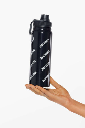 A hand with a silver index finger ring holds the Lorna Jane Iconic Insulated Water Bottle, featuring a black design, flip-top lid, secure silicone seal, and "LORNA JANE" printed in white diagonal text.