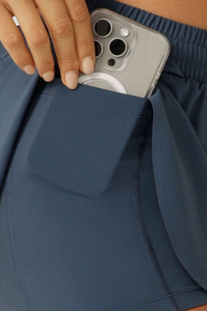 A hand places a smartphone with a clear case into the side pocket of blue Lorna Jane Lightspeed Phone Pocket Run Short, designed with sweat-wicking fabric for extra comfort.