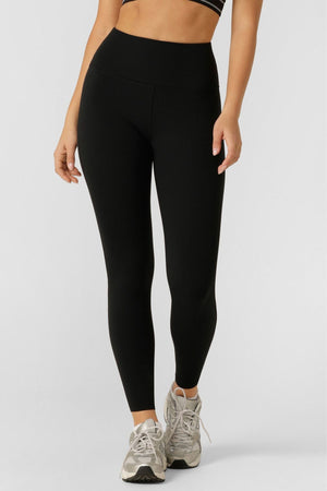 Someone models Lorna Jane Amy Thermal Phone Pocket Ankle Biter Leggings, paired with a black sports bra and gray athletic shoes, standing against a plain white background. The image is cropped to show only the lower torso and legs.