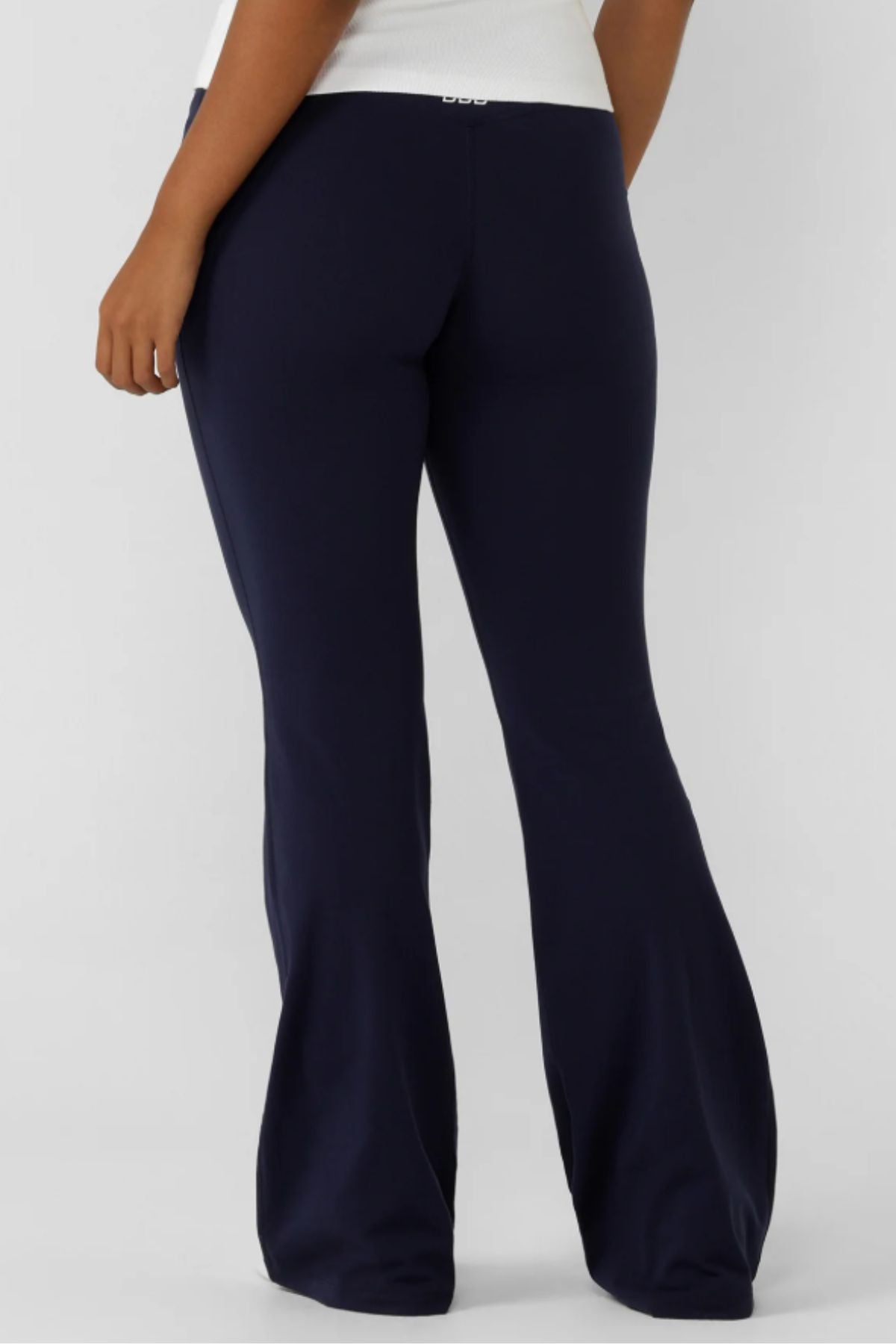 Person wearing Lorna Jane Lotus Flared Legging in dark navy blue and a white top, shown from the back against a plain light gray background.
