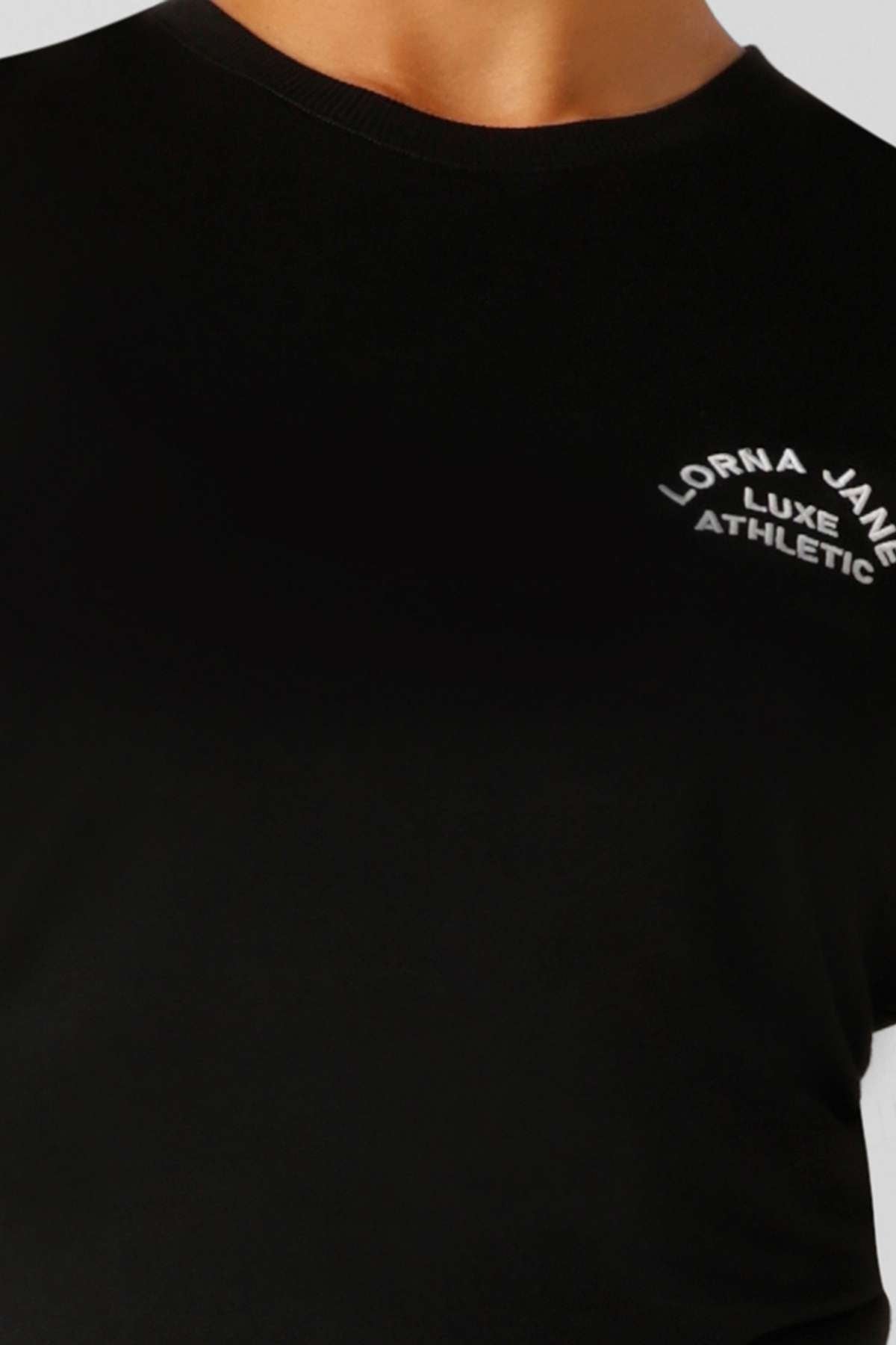 Close-up of a person wearing the Lorna Jane Lotus Muscle Tank, showing only the neck and upper torso. This black tank features “Lorna Jane Luxe Athletic” in white text on the chest, highlighting its lightweight design for easy layering.