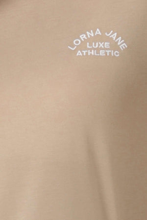 Close-up of the Lorna Jane Lotus T-Shirt’s beige fabric, showcasing its white embroidered "LORNA JANE LUXE ATHLETIC" logo arched to embody an active lifestyle.