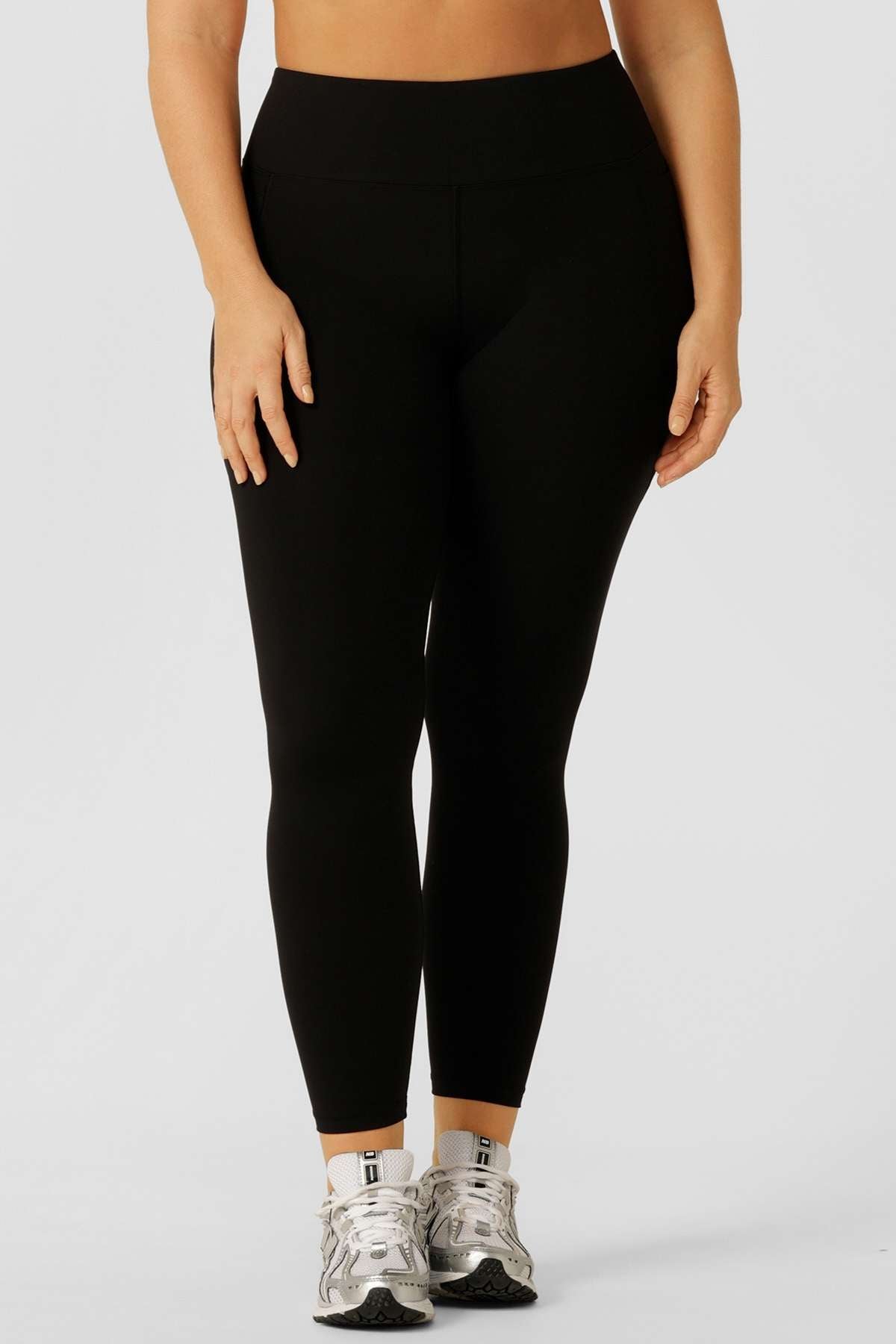 A person wears Lorna Jane Lotus Thermal No Chafe Full Length Leggings and silver athletic shoes against a plain light gray background. The image is cropped from shoulders to feet.