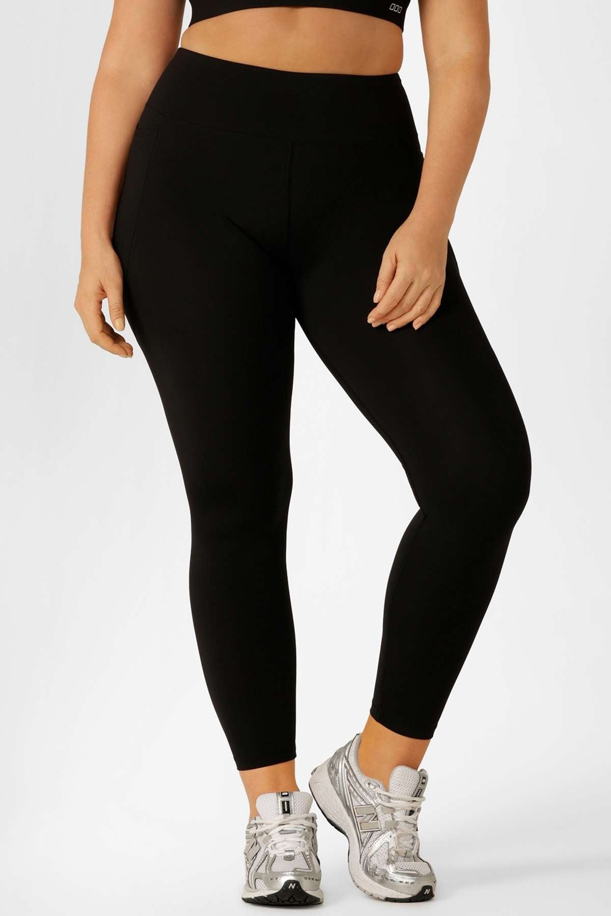 A person wearing Lorna Jane Lotus Thermal No Chafe Full Length Leggings, a black crop top, and silver athletic shoes stands against a plain white background.