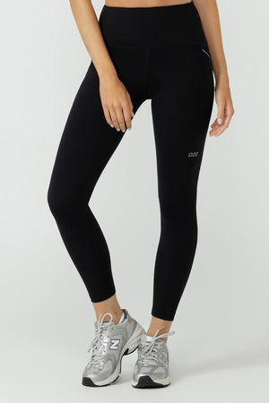 Wearing Lorna Jane Peak Performance 3 Pocket Ankle Biter Leggings and gray New Balance sneakers, a person stands against a plain light background with one hand resting on their thigh.
