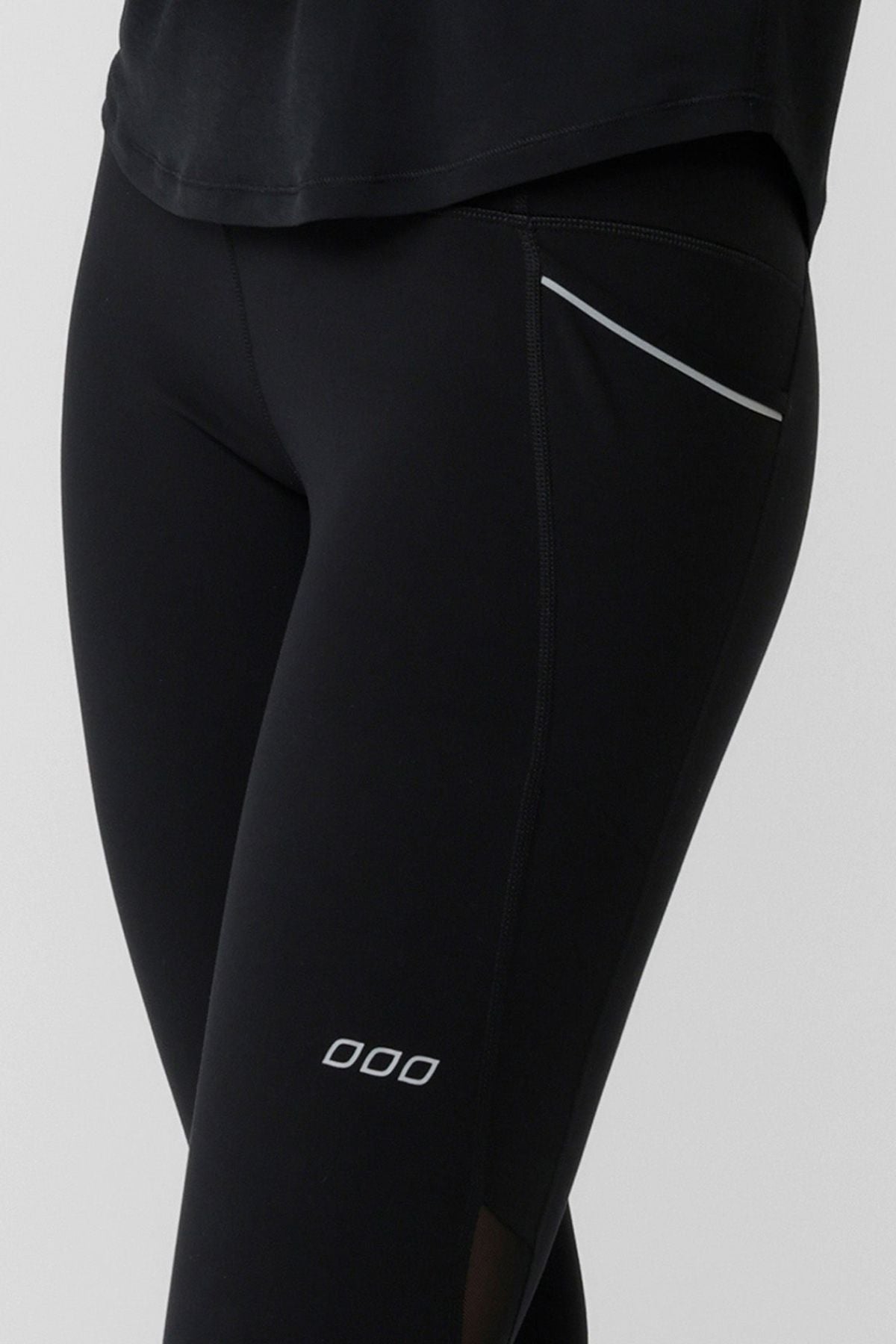 Model wearing Lorna Jane Peak Performance 3 Pocket Ankle Biter Leggings, featuring a small logo on the thigh and a reflective strip by the pocket, paired with a black shirt. Only the lower torso and upper legs are shown.