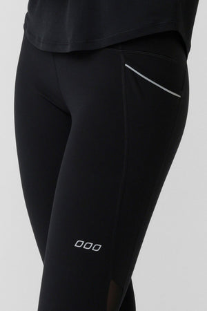 Model wearing Lorna Jane Peak Performance 3 Pocket Ankle Biter Leggings, featuring a small logo on the thigh and a reflective strip by the pocket, paired with a black shirt. Only the lower torso and upper legs are shown.