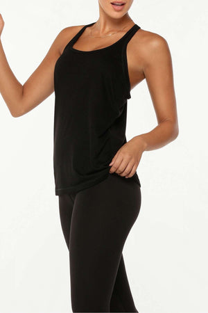 A woman wearing the Lorna Jane Slouchy Gym Tank and black leggings poses against a white background, with one arm bent and a slight smile.