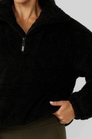 A person wears the Lorna Jane Everyday Teddy Quarter Zip Sweat with one hand in their pocket. Only their lower face, torso, and one arm are visible against a light gray background.
