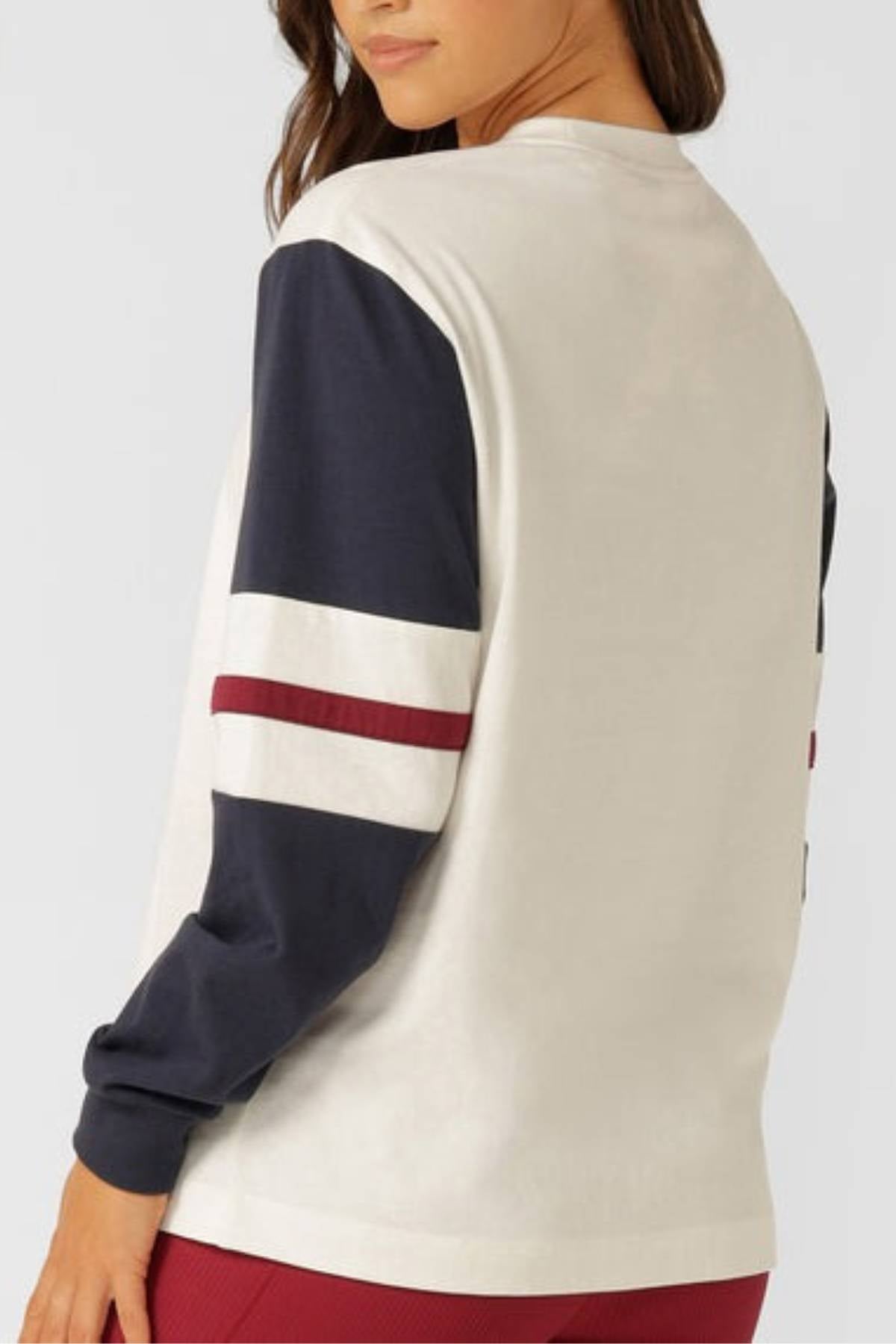 A person shown from the back and side wearing red pants and the Lorna Jane Varsity Long Sleeve T-Shirt in breathable cotton with navy sleeves, white and maroon stripes.