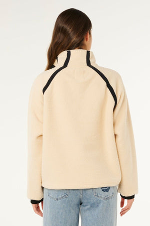 A person with long brown hair, viewed from behind, is wearing the Rip Curl Surf Club Heritage Polar jacket in cream with black trim, paired with light blue jeans. The background is plain white.