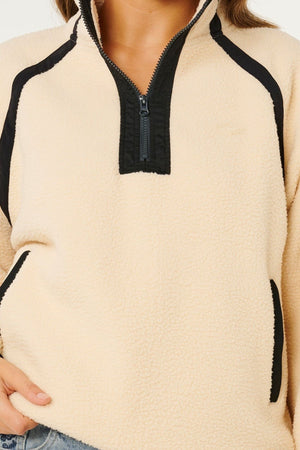 A person wearing the Rip Curl Surf Club Heritage Polar, a cream-colored fleece pullover with black trim, classic surf style design, zippered collar, and side pockets. Only the torso and part of one hand are visible.