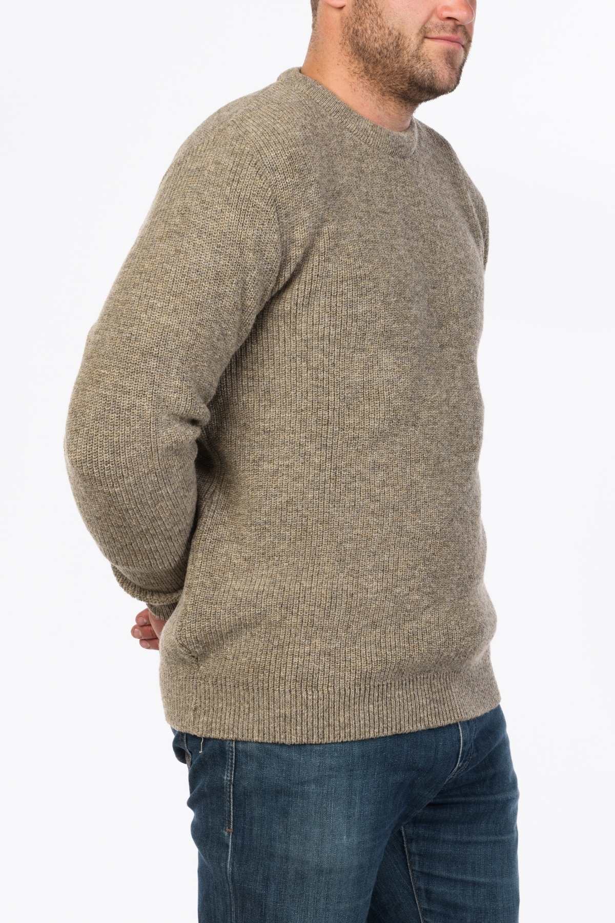 A man in the MKM Original Backyard Knit beige wool pullover and blue jeans stands against a plain white background, showcasing relaxed casual wear with his hands behind his back.