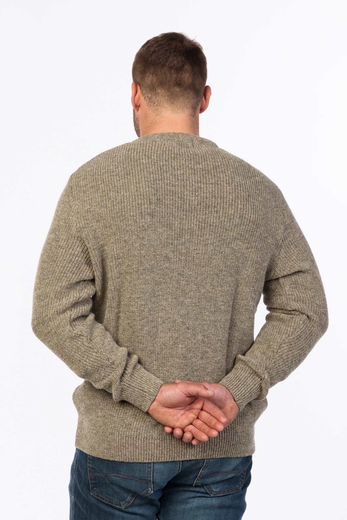 A man in an MKM Original Backyard Knit pullover and blue jeans stands with his back to the camera, hands clasped behind him, against a plain white background, embodying effortless casual wear.