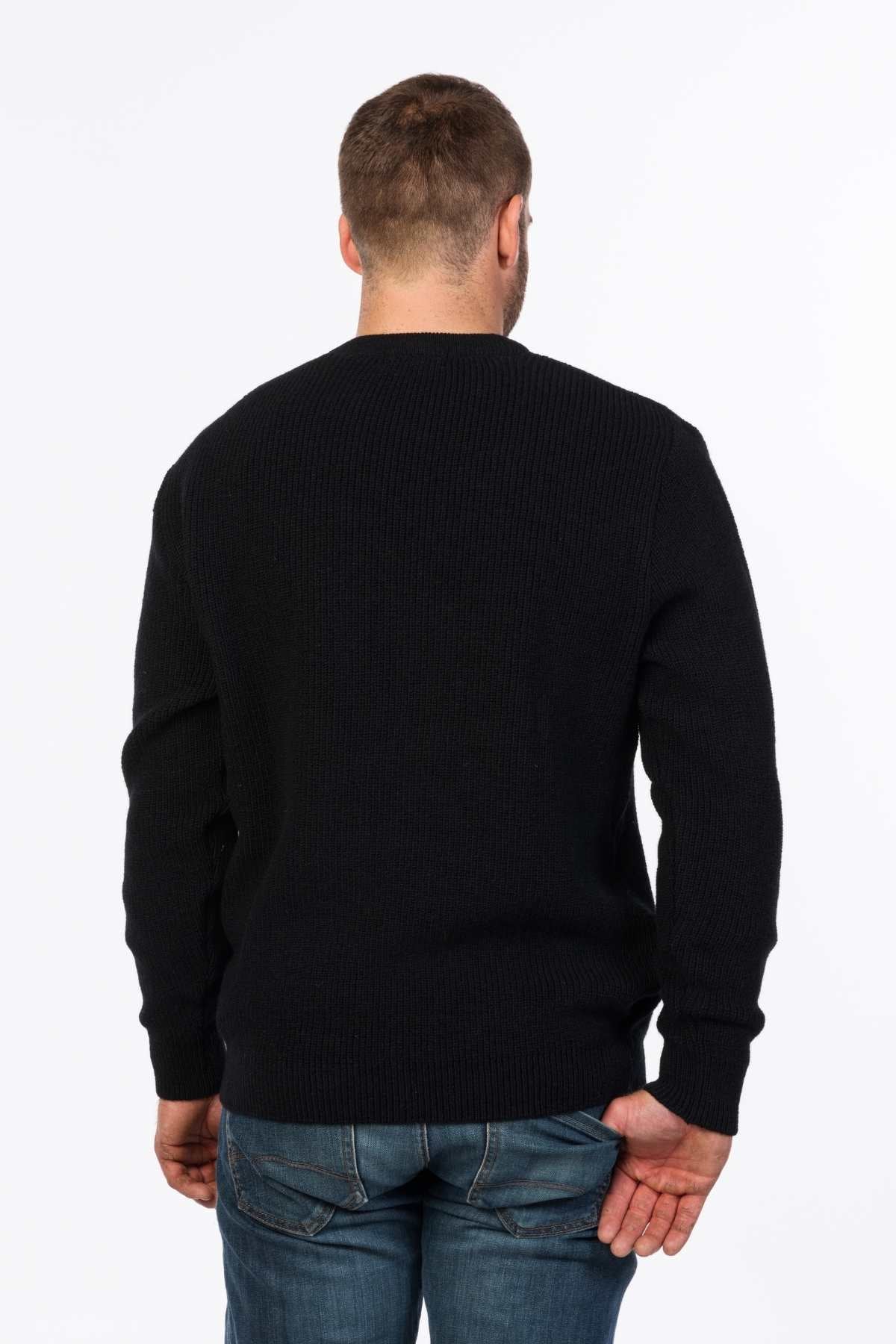 A man with short hair, wearing a black ribbed MKM Original Backyard Knit pullover and blue jeans, stands with his back to the camera against a plain white background.