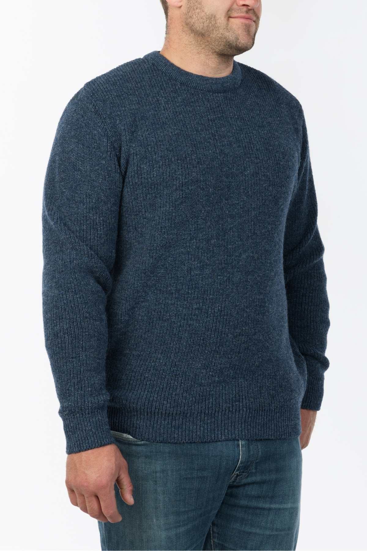 A person in an MKM Original Backyard Knit pullover and jeans stands against a plain white background, effortlessly embodying the charm of classic New Zealand style.