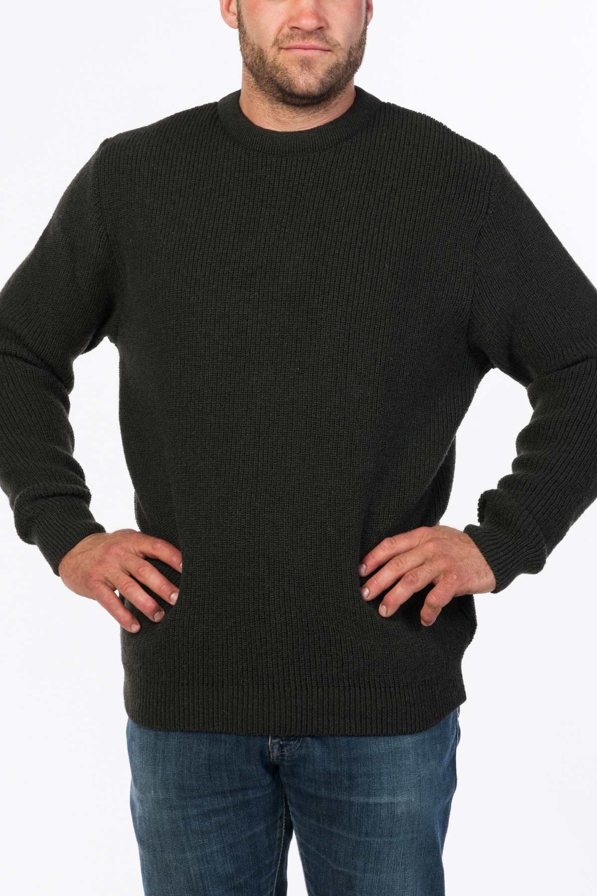 A person stands confidently with their hands on their hips, wearing the MKM Original Backyard Knit crafted in New Zealand and blue jeans. The plain white background highlights the casual wear ensemble.