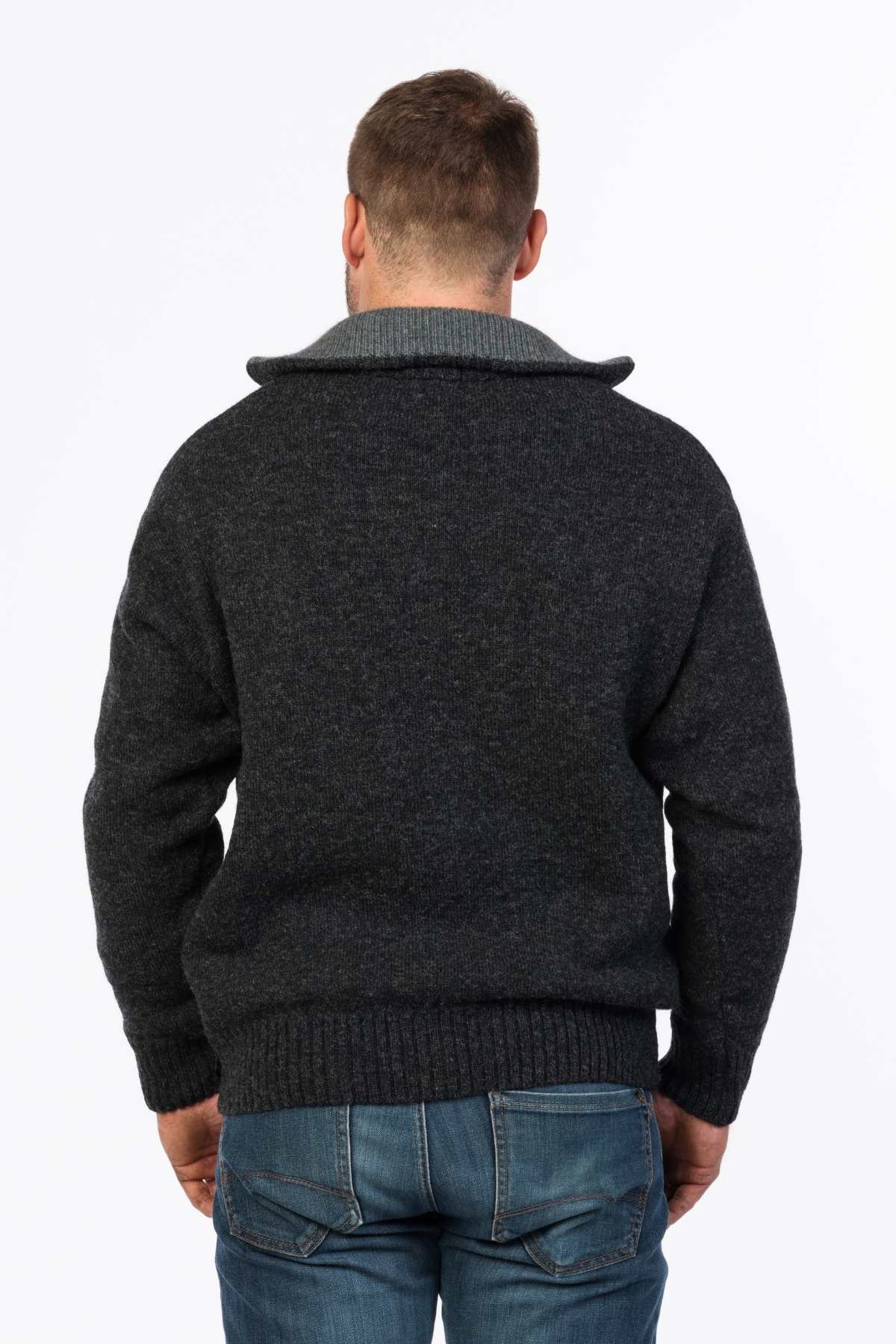 A back view of a person wearing a dark gray MKM Tasman Dual Layer Possum & Merino Knit sweater with a light gray collar, paired with blue jeans. The person has short hair and appears to be standing against a plain white background.