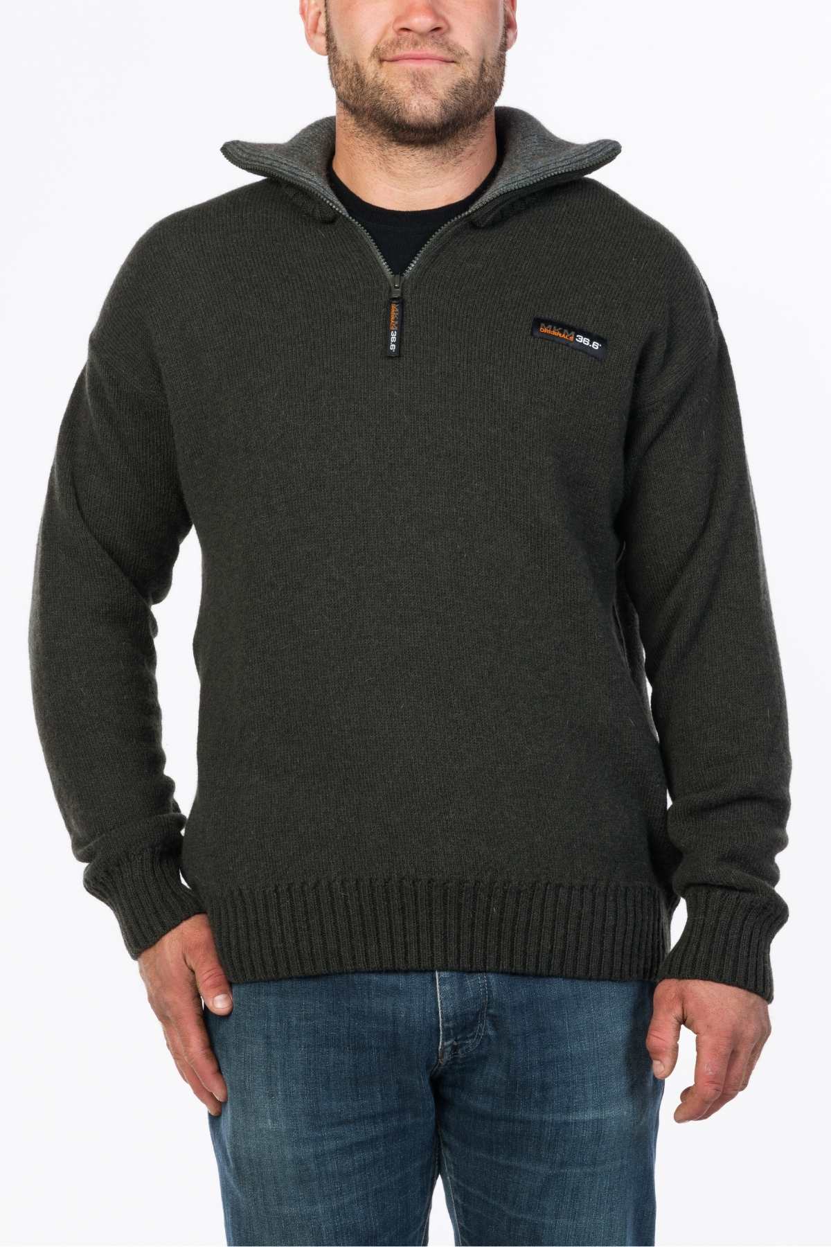 A man wearing an MKM Tasman Dual Layer Possum & Merino Knit, dark green quarter-zip sweater stands against a white background. The New Zealand-made sweater features ribbed collar, cuffs, hem, and a small logo patch on the left chest. His hands rest casually in his jeans pockets.