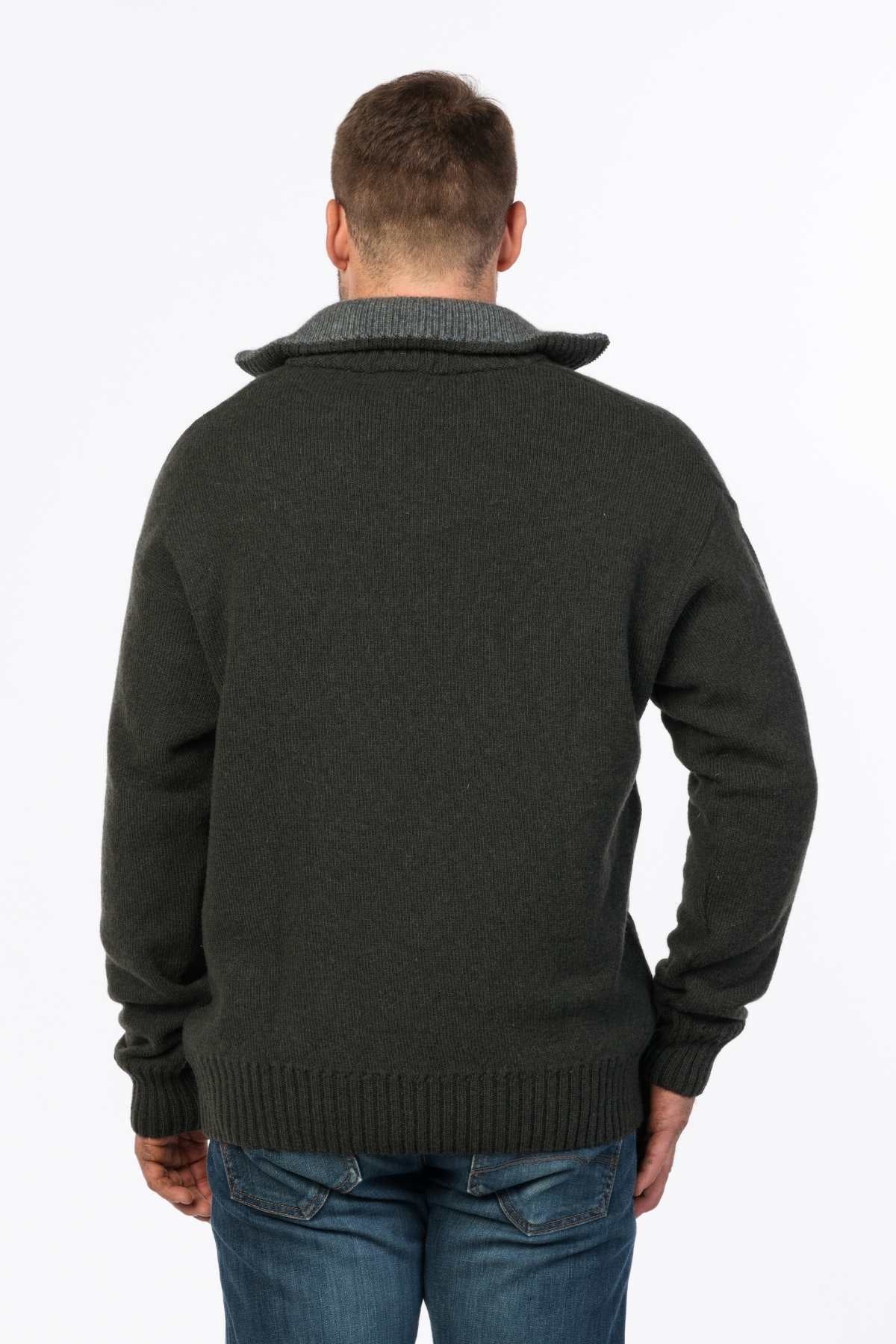 A person is standing with their back to the camera, wearing a dark gray MKM Tasman Dual Layer Possum & Merino Knit sweater with a high collar, paired with blue jeans. The background is plain white.