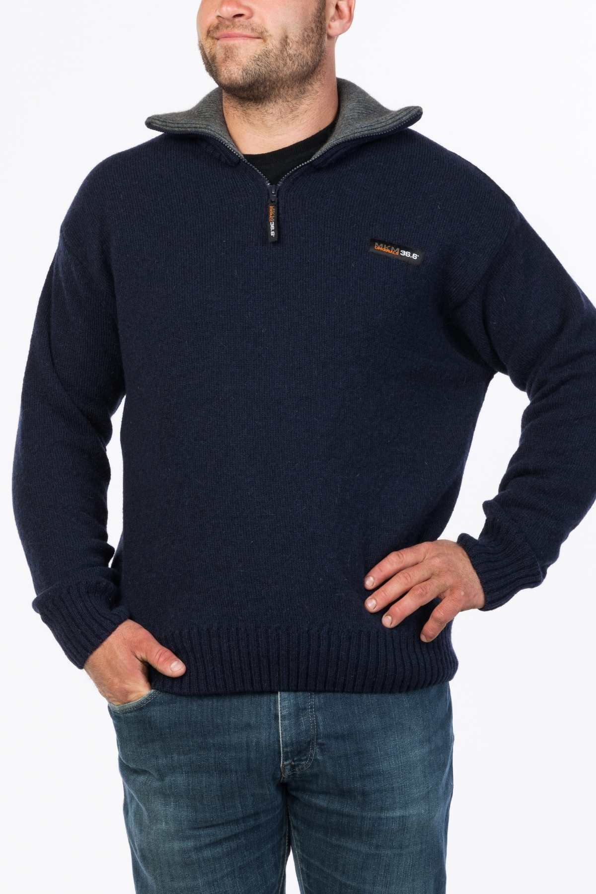 A man wears the MKM Tasman Dual Layer Possum & Merino Knit, a dark blue zip-up sweater with a gray inner collar, paired with blue jeans, standing against a white background.