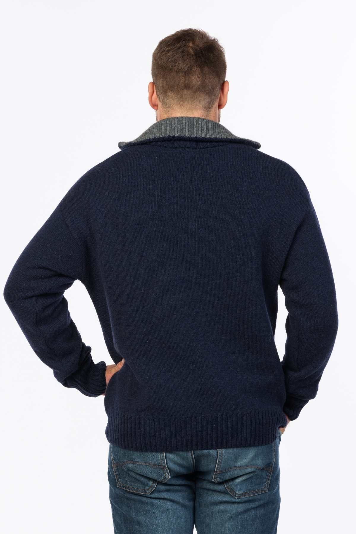 A man poses with his back to the camera in a MKM Tasman Dual Layer Possum & Merino Knit sweater featuring a gray collar, paired with blue jeans. His hands rest on his hips against a plain white background.