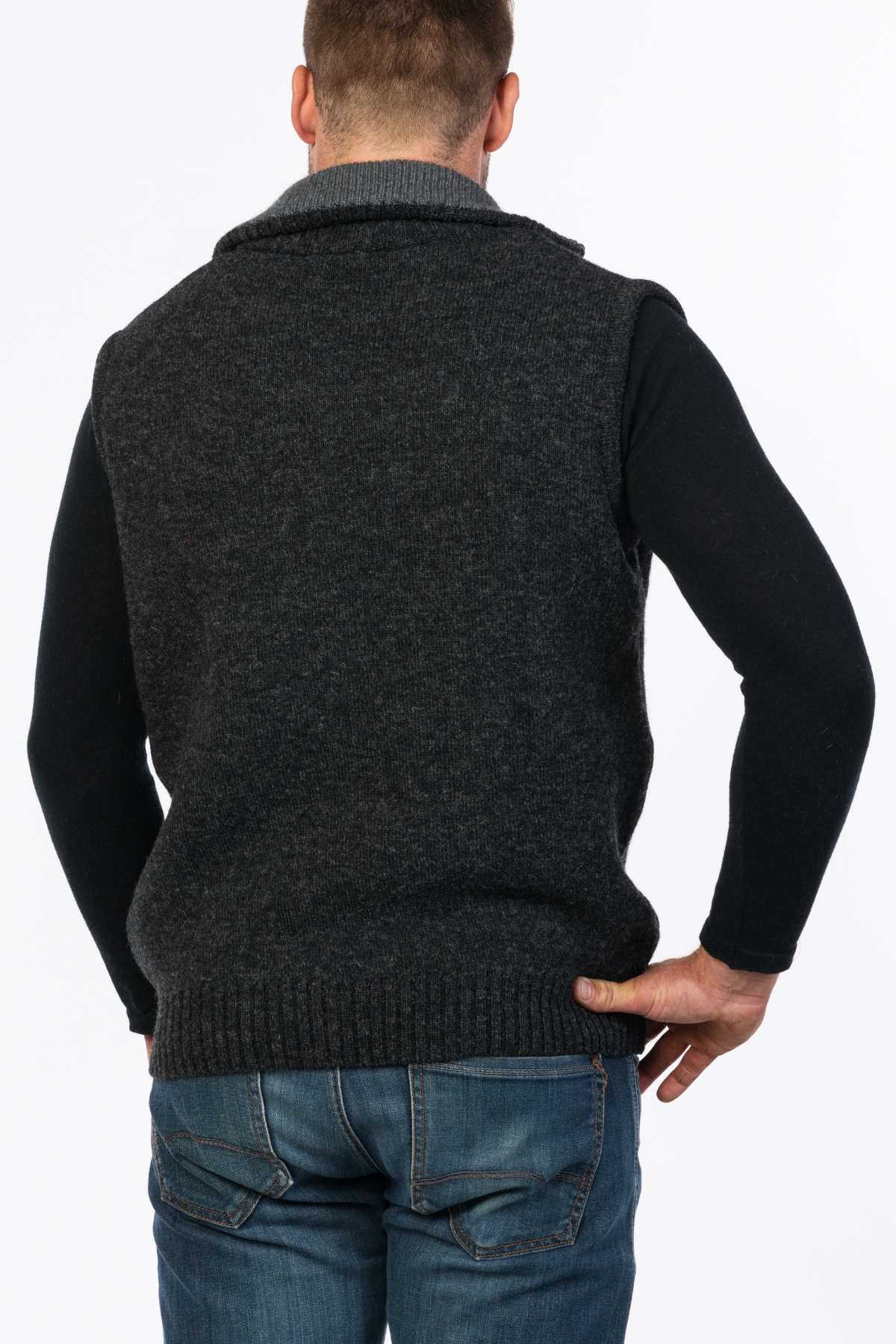 A person wearing an MKM Tasman Vest Dual Layer Possum & Merino over a long-sleeve black shirt with blue jeans stands with their back to the camera.