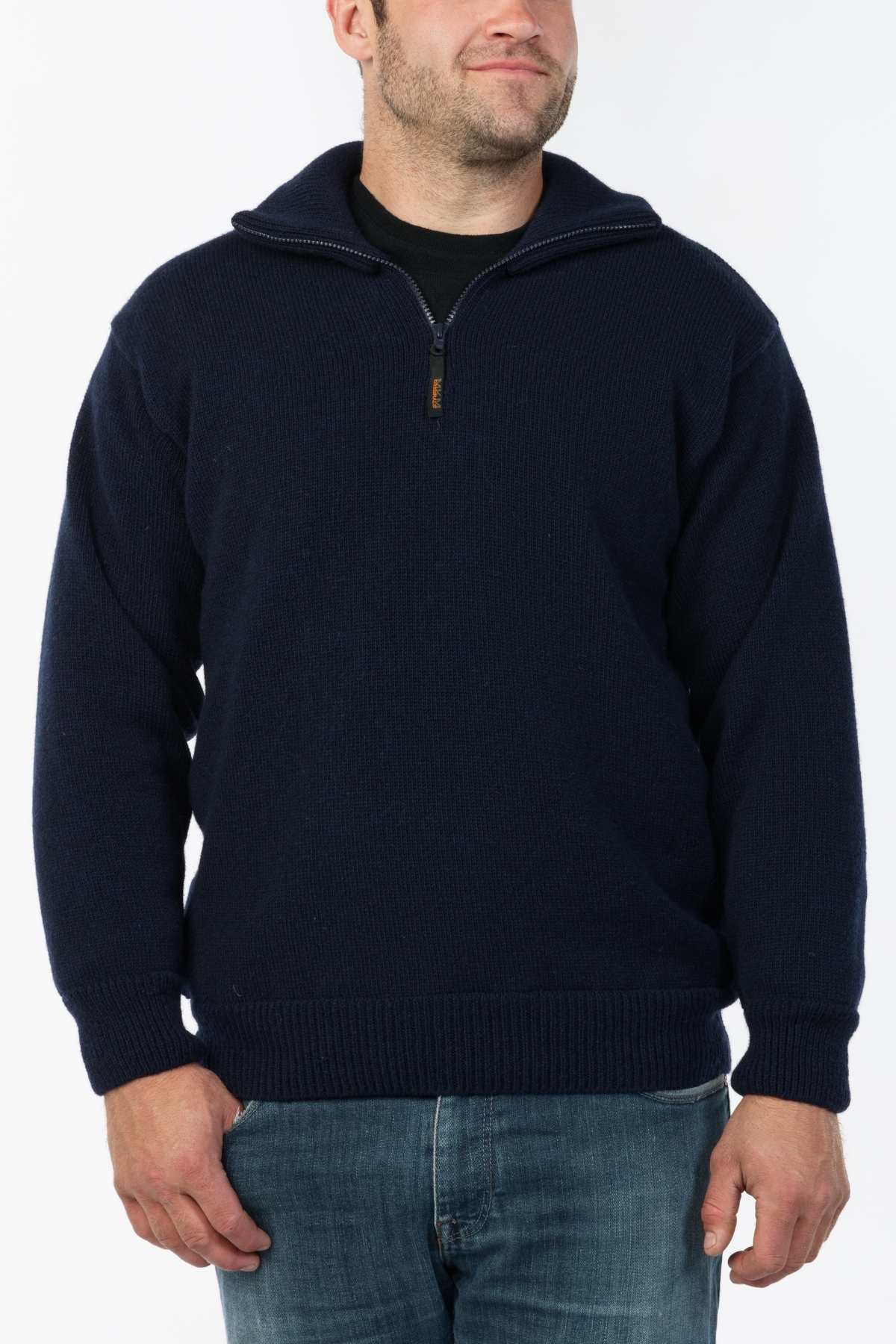 A man wearing the MKM Windbreaker Knit, a navy blue 100% wool jumper, over a black shirt and blue jeans stands against a plain white background, smiling slightly.