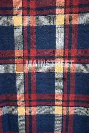 A close-up of the Milton Open Front Flannelette Shirt shows its plaid pattern in blue, red, white, and yellow stripes with "MAINSTREET" printed boldly in white across the center.