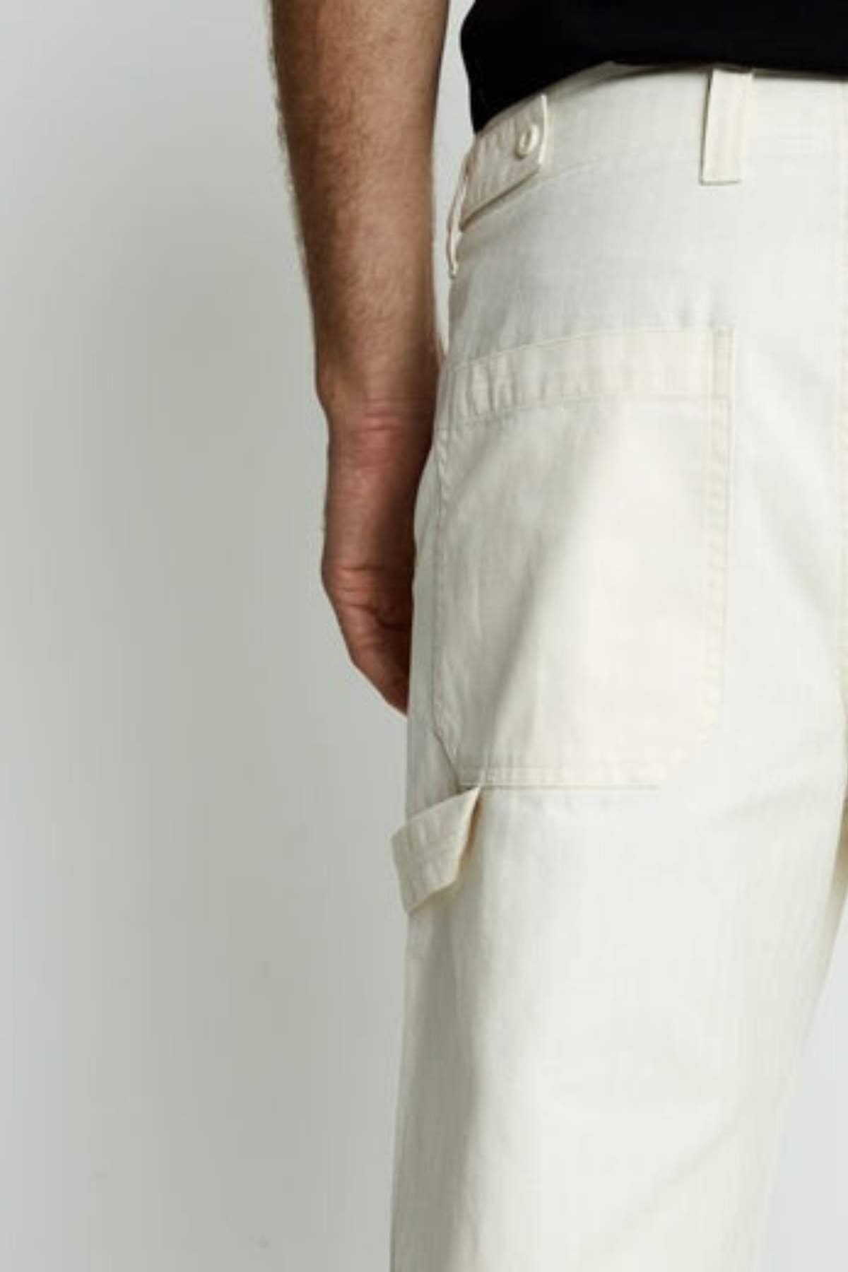 A person is shown from the waist down, standing with one arm relaxed by their side, wearing Mr Simple Carpenter Pant in beige and a black shirt against a plain background.