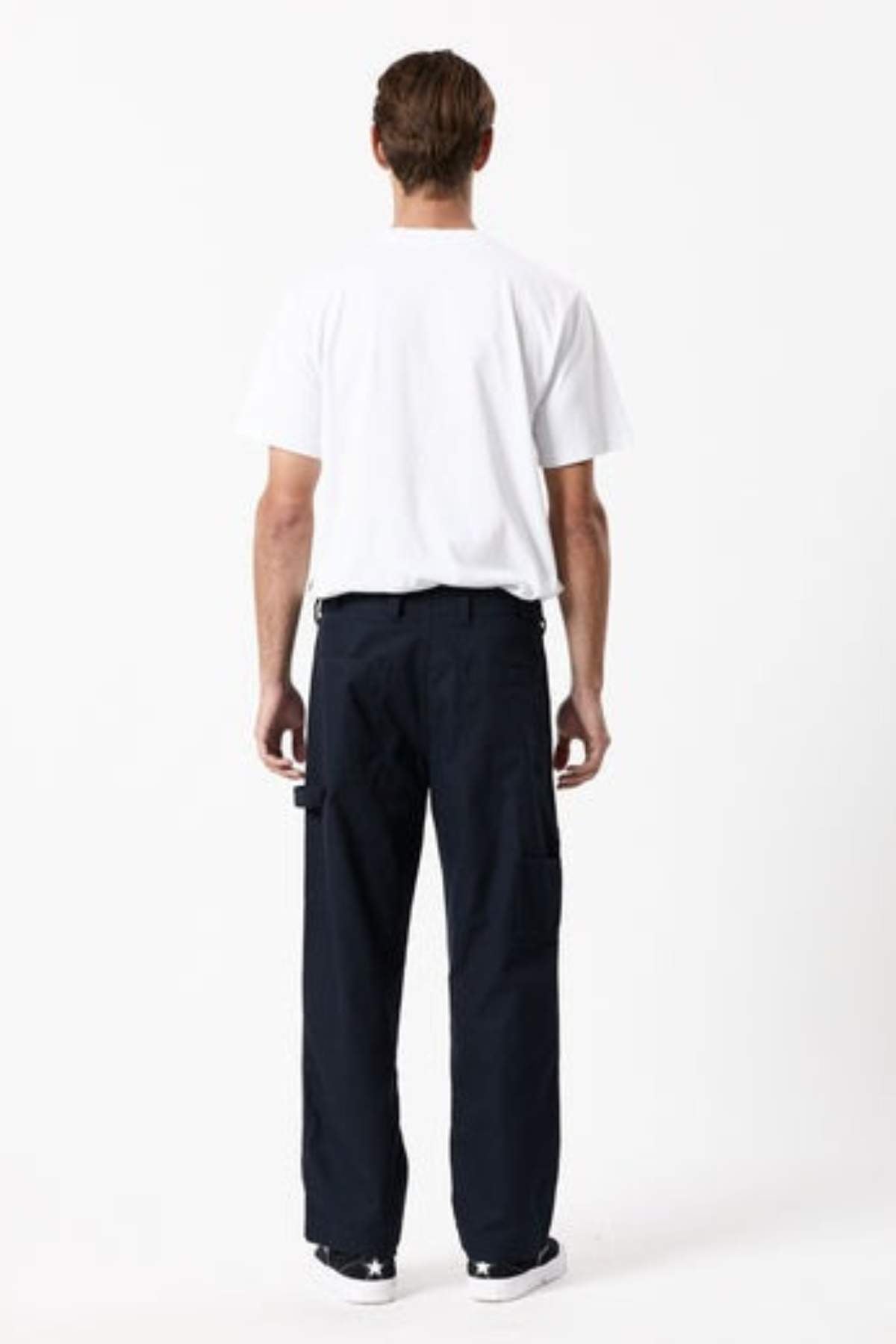 A person stands facing away from the camera, wearing a plain white t-shirt, Mr Simple Carpenter Pant with a workwear-inspired relaxed fit, and black sneakers with white soles against a plain white background.