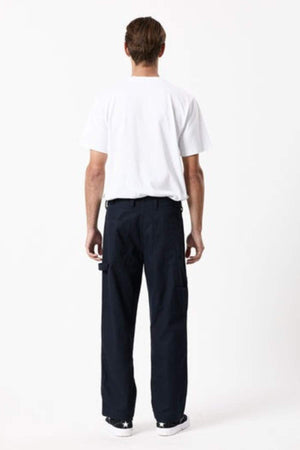 A person stands facing away from the camera, wearing a plain white t-shirt, Mr Simple Carpenter Pant with a workwear-inspired relaxed fit, and black sneakers with white soles against a plain white background.