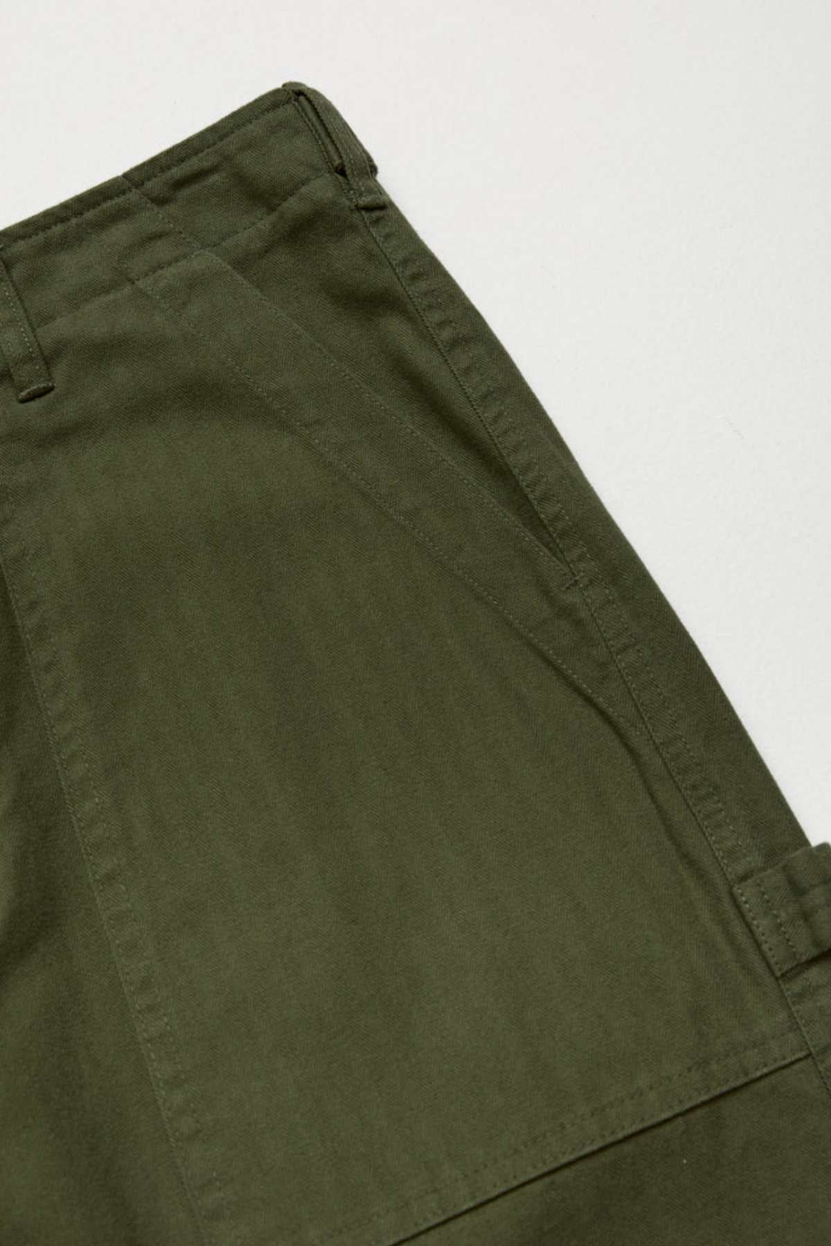 Close-up of Mr Simple Carpenter Pant in olive green, featuring the waistband, belt loop, and side pocket. The workwear-inspired design showcases textured 100% cotton fabric and detailed stitching against a plain light background.