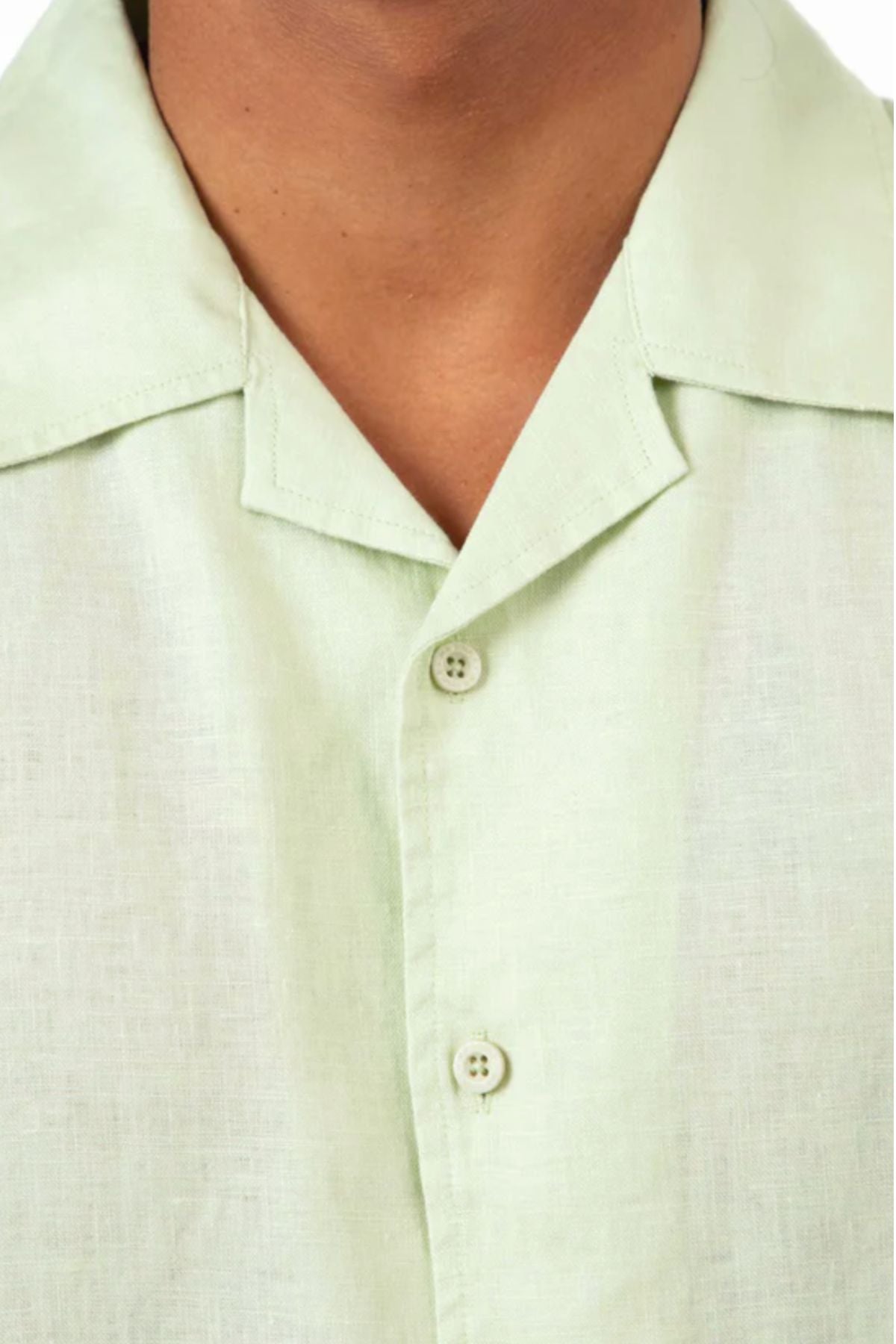 Close-up of a person wearing the Mr Simple Cuban Linen Short Sleeve Shirt in pale green, featuring lightweight linen, a notched collar, and two visible buttons. The shot shows the lower face and neck, with most facial features out of frame.