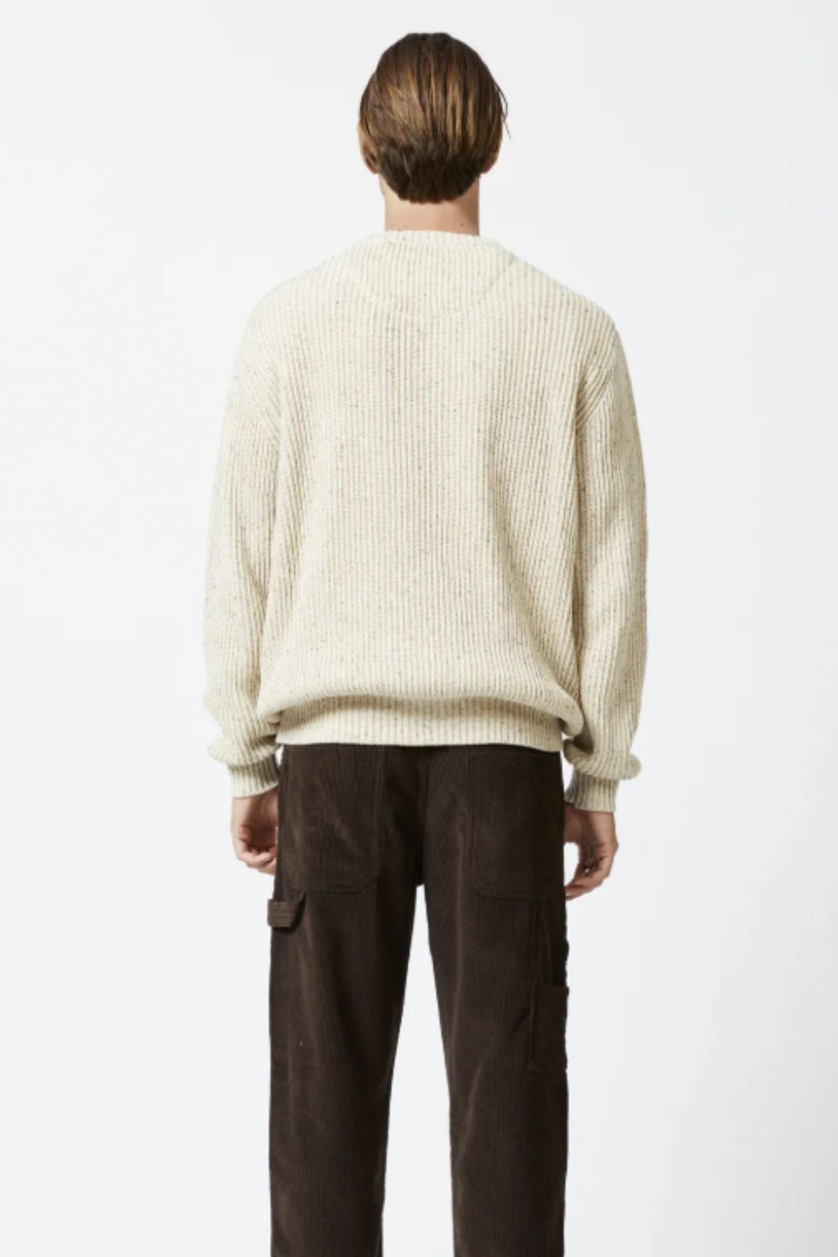 Facing away, a person wears the Mr Simple Fisher Knit—a cream-colored, relaxed fit sweater crafted from organic cotton—paired with dark brown cargo pants against a plain white background.